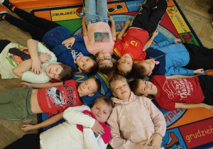 Chłopcy z klasy trzeciej B pozują leżąc na dywanie tworząc koło, z różowym szalikiem